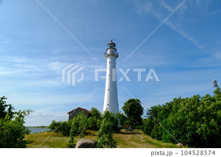 Kihnu island lighthouse in Estonia. Stand alone single white lighthouse stones green forest summer blue sky. Kihnu island lighthouse in Estonia. Stand alone single white lighthouse stones green forest summer blue sky. 104528574