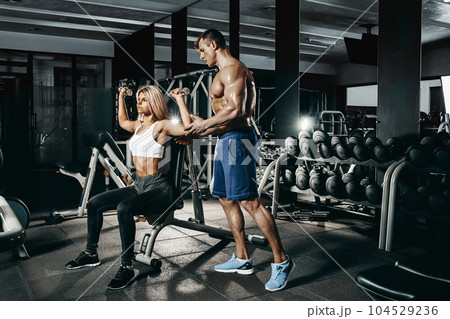 Fitness instructor exercising with his client at the gym. 104529236
