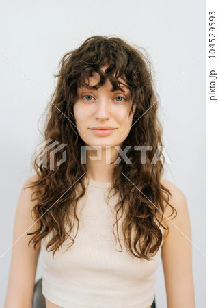 Vertical studio portrait of pretty young woman before applying professional makeup and making stylish hairstyle standing on isolated white background, looking at camera. Concept of fashion and beauty Vertical studio portrait of pretty young woman before applying professional makeup and making stylish hairstyle standing on isolated white background, looking at camera. Concept of fashion and beauty 104529593