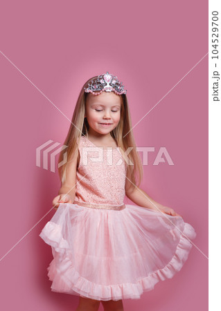 Cute child girl in elegant pink dress and tiara celebrates birthday party on pink background. 104529700