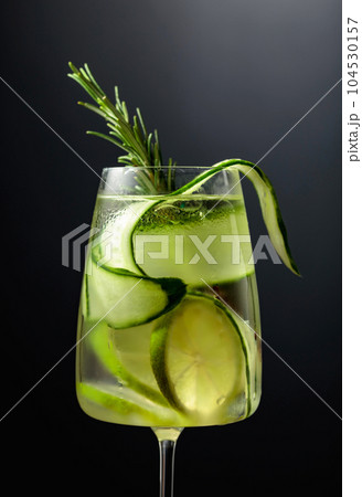 Gin tonic with ice, rosemary, lime, and cucumber in frosted glass on a black background. 104530157