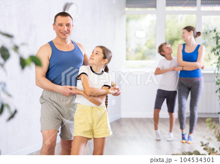 Positive preteen girl exercising dance moves with father during dance class, family practicing dance in pairs in studio 104534301