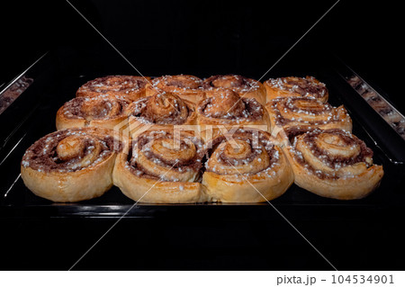 Twelve baked cinnamon buns on tray in electric oven at home Twelve baked cinnamon buns on tray in electric oven at home 104534901