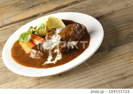 クレソン、人参、ジャガイモの付け合わせとクリームがかかっている厚切り牛タンのビーフシチュー 104535728