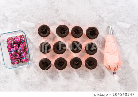 Flat lay. Piping strawberry buttercream frosting on top of chocolate cupcakes. Flat lay. Piping strawberry buttercream frosting on top of chocolate cupcakes. 104540347