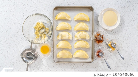 Flat lay. Brushing uncooked breakfast empanadas with eggs and sweet potato with egg wash. 104540666