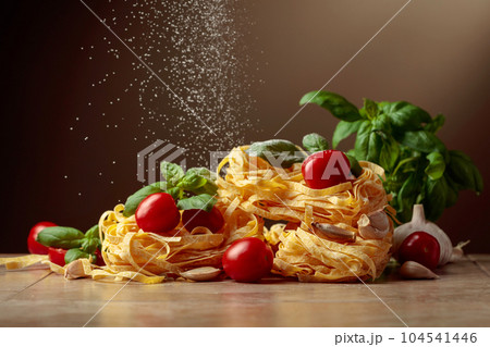 Homemade raw pasta with tomato, garlic, and basil on a brown background. 104541446