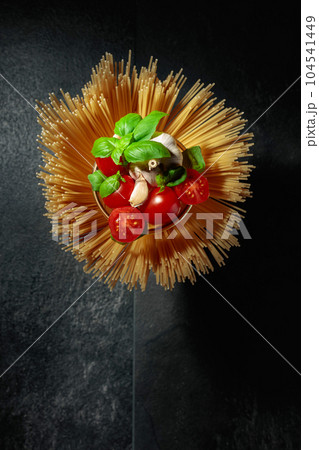 Raw spaghetti with tomato, garlic, and basil on a black stone table. 104541449