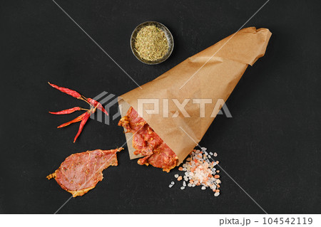Overhead view of dried pork jerky in parchment bag with salt and chilli pepper Overhead view of dried pork jerky in parchment bag with salt and chilli pepper 104542119