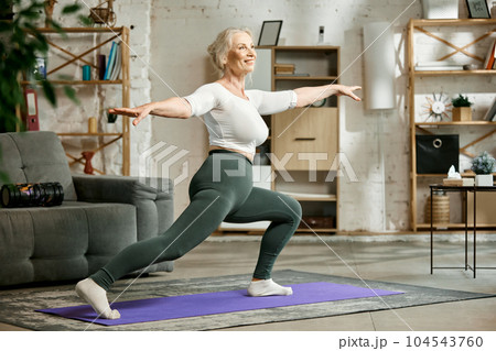 Beautiful, active, senior woman training at home in lion room, doing stretching and yoga exercises. Toned body, energy 104543760