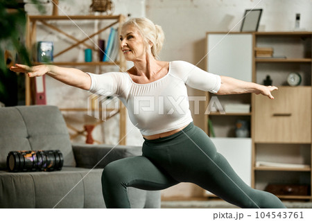 Beautiful, active, senior woman training at home in lion room, doing stretching and yoga exercises. Toned body, energy 104543761