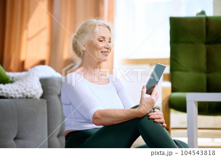 Beautiful, smiling, senior woman in sportswear looking on phone, watching online sport videos for training at home Beautiful, smiling, senior woman in sportswear looking on phone, watching online sport videos for training at home 104543818