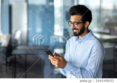 Young successful mature businessman inside the office using the phone, man holding a smartphone online application user, smiling browsing the internet and dialing a call. 104549031