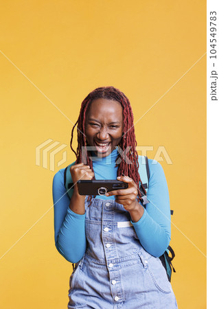 Joyful woman enjoying videogames win, playing mobile games online in studio. Female traveller having fun with shooter gaming challenge on smartphone app, journey trip destination. Joyful woman enjoying videogames win, playing mobile games online in studio. Female traveller having fun with shooter gaming challenge on smartphone app, journey trip destination. 104549783