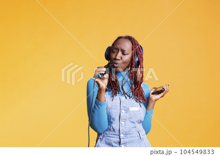 Confident girl having fun with karaoke, vocalist singing songs on camera to show talent. Young female singer artist creating beautiful performance live in studio, using microphone. 104549833