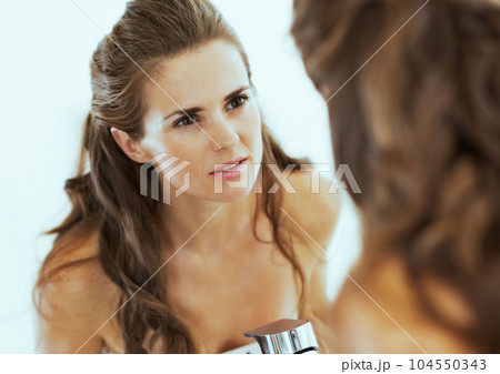 Concerned young woman looking in mirror Concerned young woman looking in mirror 104550343