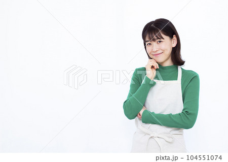 白い背景の前で笑顔で考えているエプロン姿の30代主婦 104551074