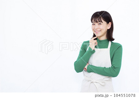 白い背景の前で笑顔で考えているエプロン姿の30代主婦 104551078