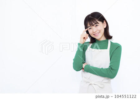 白い背景の前で笑顔で考えているエプロン姿の30代主婦 104551122
