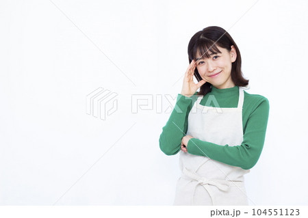 白い背景の前で笑顔で考えているエプロン姿の30代主婦 白い背景の前で笑顔で考えているエプロン姿の30代主婦 104551123