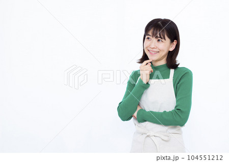 白い背景の前で笑顔で考えているエプロン姿の30代主婦 白い背景の前で笑顔で考えているエプロン姿の30代主婦 104551212