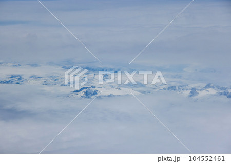 Amidst clouds majestic Greenland mountain peaks emerge adorned with blanket of glistening snow Amidst clouds majestic Greenland mountain peaks emerge adorned with blanket of glistening snow 104552461