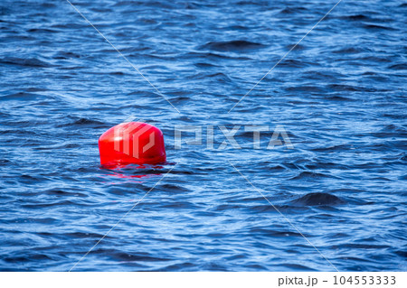 Red spherical buoy floating on blue sea water Red spherical buoy floating on blue sea water 104553333