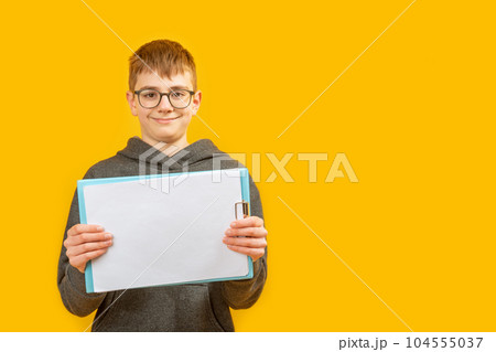 Teenager brunet boy in glasses on yellow background holds blank sheets of paper. Advertising, place for text. Copy space, mock up Teenager brunet boy in glasses on yellow background holds blank sheets of paper. Advertising, place for text. Copy space, mock up 104555037