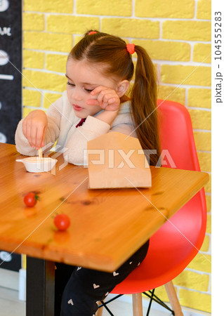A small and beautiful girl is eating french fries in a cafe. A small and beautiful girl is eating french fries in a cafe. 104555283