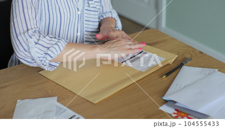 Close up female hands putting letter in envelop return form. Woman sends a return form by letter. Close up female hands putting letter in envelop return form. Woman sends a return form by letter. 104555433