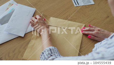 Close up female hands putting letter in envelop return form. Woman sends a return form by letter. 104555439