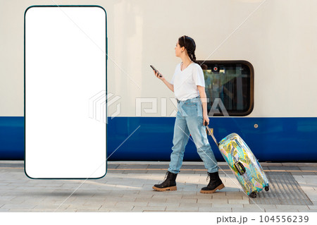Side view of young woman walking with her luggage using cellphone. Tarin in background. Big smartphone with mock up and copy space. Concept of travel and business trip. Side view of young woman walking with her luggage using cellphone. Tarin in background. Big smartphone with mock up and copy space. Concept of travel and business trip. 104556239