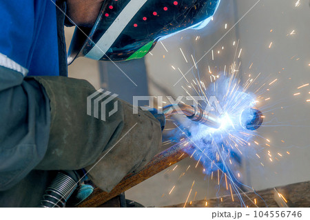 Masked welder works in workshop and sparks fly. Close-up portrait. Industrial background. Authentic Masked welder works in workshop and sparks fly. Close-up portrait. Industrial background. Authentic 104556746