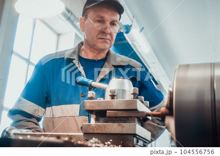 Professional metal turner works at factory on lathe. Portrait of turner at work in turning workshop 104556756