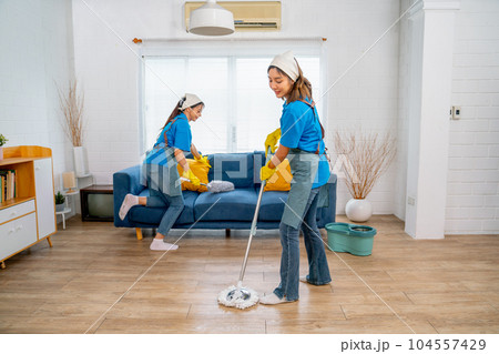 Asian housemaid or housekeeper team help to clean living room together with one use mop clean floor Asian housemaid or housekeeper team help to clean living room together with one use mop clean floor 104557429