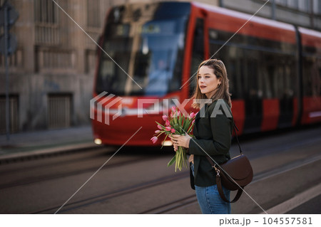 Portrait of young woman in city with bouquet of tulips. 104557581