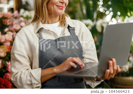 Close up of florist wearing apron working on laptop and taking online orders in store Close up of florist wearing apron working on laptop and taking online orders in store 104560423