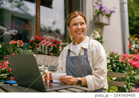 Professional flower shop owner florist using laptop and writing on notebook at flower shop Professional flower shop owner florist using laptop and writing on notebook at flower shop 104560460