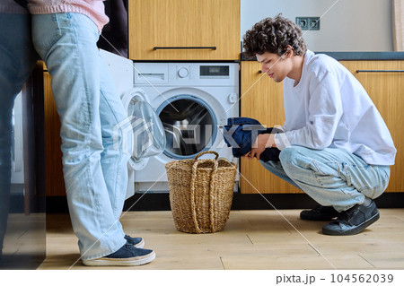 Young guy at home using washing machine with basket of dirty things 104562039