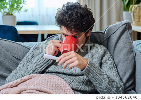 Young guy checking temperature, lying on couch under blanket 104562040