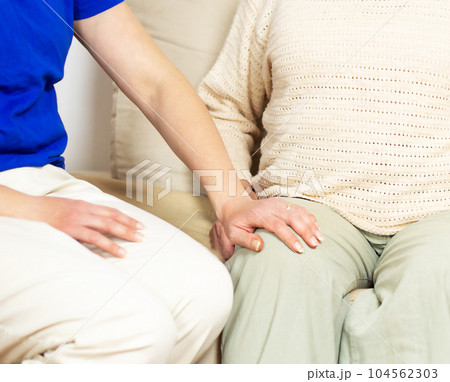 Young caregiver helping senior woman with knee pains at home. Caring nurse assisting her patient. Young caregiver helping senior woman with knee pains at home. Caring nurse assisting her patient. 104562303