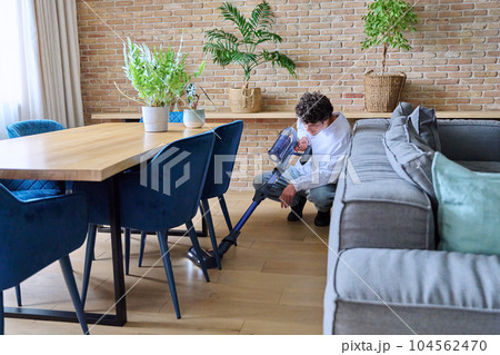 Young guy doing vacuuming, at home in the living room 104562470