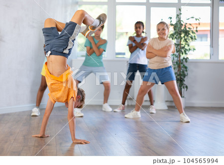 Positive juvenile boy engaged in Breakdancing in training room with children's group 104565994