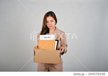 Sad young businesswoman holding a box full of her stuff, feeling sad after quitting her job 104570290