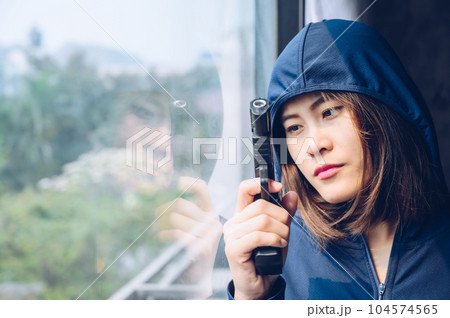 Female criminal (or thief) wearing hood and looking thought window for waiting her victim. Female criminal (or thief) wearing hood and looking thought window for waiting her victim. 104574565