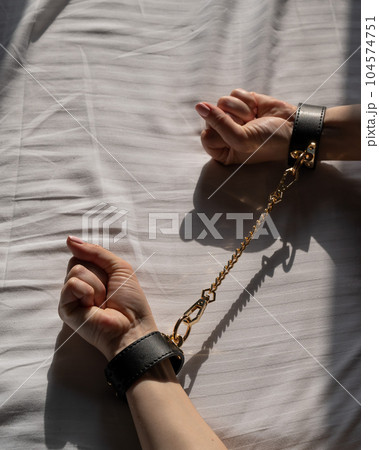 Close-up of woman's hands in leather handcuffs. Sex toy. Close-up of woman's hands in leather handcuffs. Sex toy. 104574751