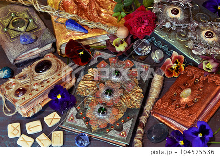 Still life with magic book of spells and fairy tales, runes and flowers on the table. Occult, esoteric and witchcraft concept. Mystic background with vintage objects Still life with magic book of spells and fairy tales, runes and flowers on the table. Occult, esoteric and witchcraft concept. Mystic background with vintage objects 104575536