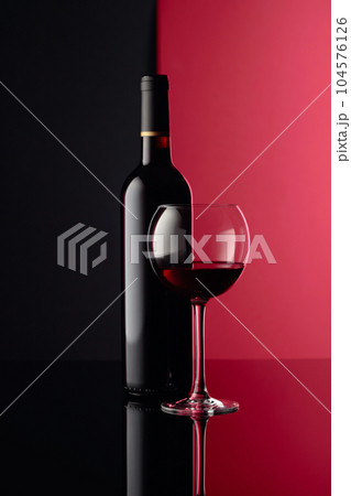 Glass and bottle of red wine on a black reflective background. Copy space. 104576126