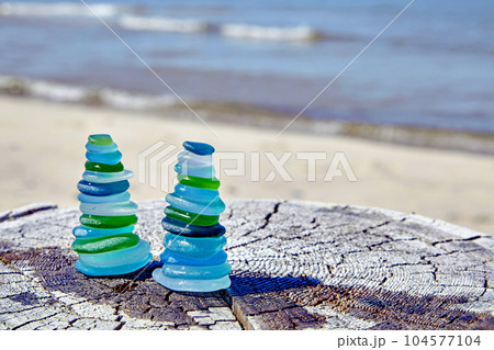 two balanced pyramids of sea-polished glass bottle shards on a weathered wooden surface against the backdrop of the sea 104577104