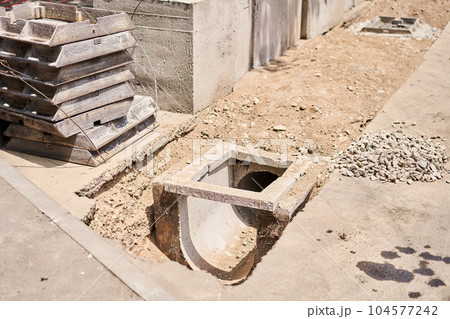 Laying concrete manholes and drain pipes for stormwater system. Connecting a trench drain to a concrete manhole structure at construction site. Construct stormwater and underground utilities Laying concrete manholes and drain pipes for stormwater system. Connecting a trench drain to a concrete manhole structure at construction site. Construct stormwater and underground utilities 104577242